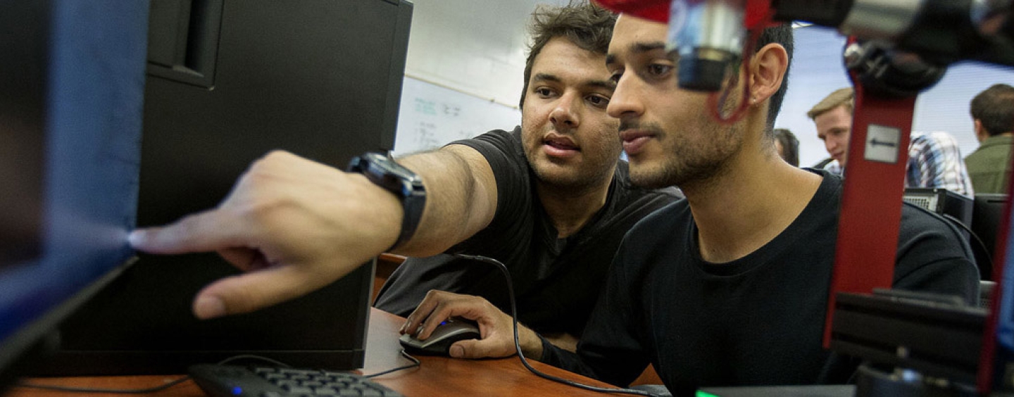 students in a lab, one pointing to a computer monitor