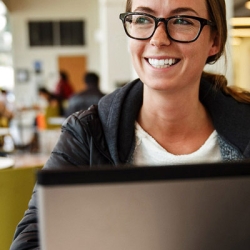 smiling student on laptop in JPLL lobby cafe